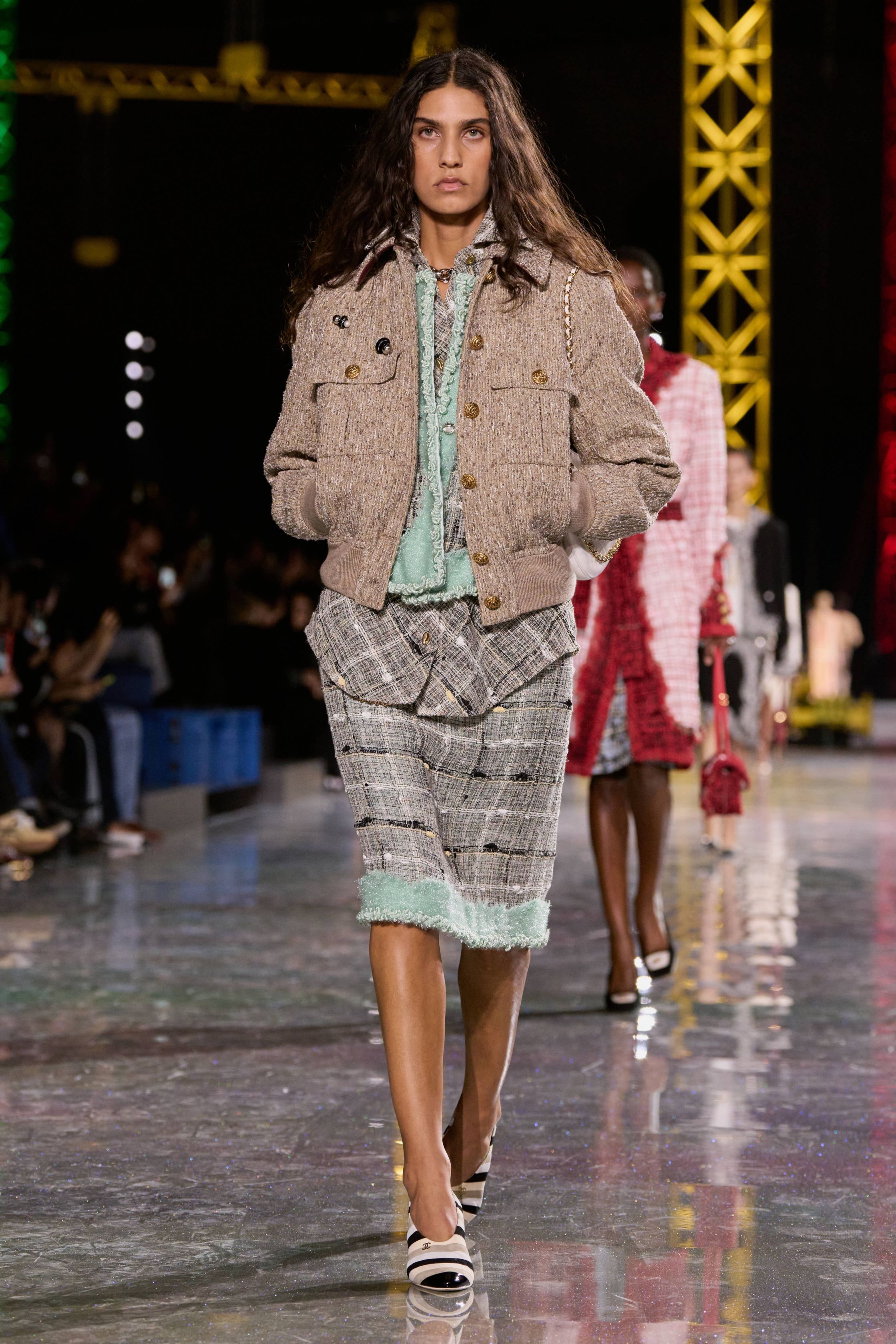 Chanel 2026秋冬在金属结构的秀场中重申品牌经典语言：斜纹软呢套装、短外套、膝下裙与珍珠配饰贯穿始终，柔粉、米色、黑白格纹与酒红色调构建出典型的巴黎优雅衣橱。本季轮廓更偏向轻松化比例，短夹克与宽松半裙形成现代化节奏，粗花呢被重新演绎为更轻盈的织物结构，同时融入羽毛、透明层纱与亮片细节，使经典香奈儿套装在年轻语境下焕发新的活力-顽石频道趋势研究